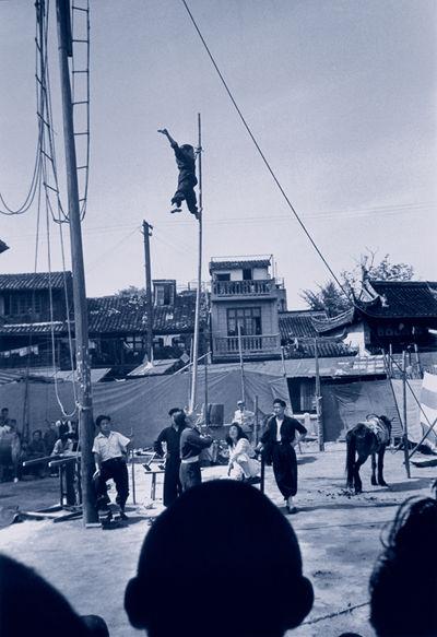 一位杂耍艺人在竹竿上表演平衡动作。（1948年5月，上海）