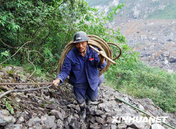 6月11日，一名工人背着救援装备在陡峭的山坡上开辟出来的通道上行进。